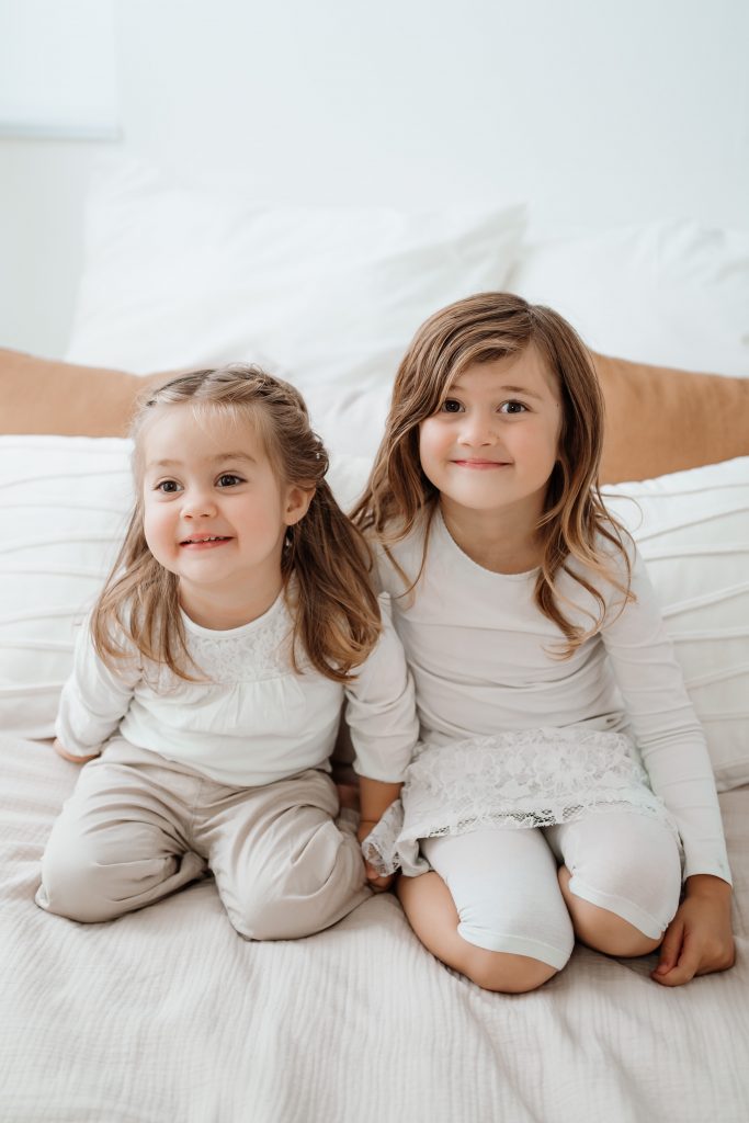 Zwei kleine Kinder sitzen nebeneinander auf einem Bett und lächeln – natürliche Familienfotografie in Singen und Waldshut-Tiengen