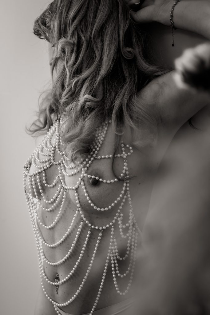 Intimes Porträt in Schwarzweiß: Rückenansicht mit Perlen-Accessoire, weiche Schatten, ruhige Stimmung.
