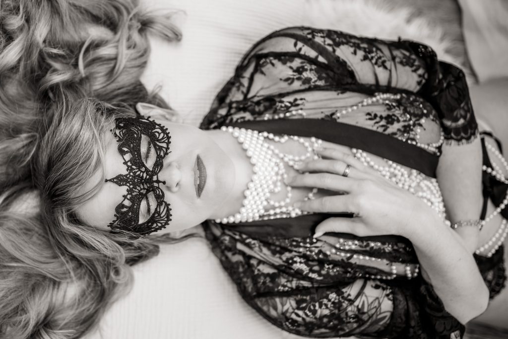 Intime Porträts in Schwarzweiß: Frau liegt mit Spitze, Maske und Perlen, weiches Licht, ruhige Eleganz.